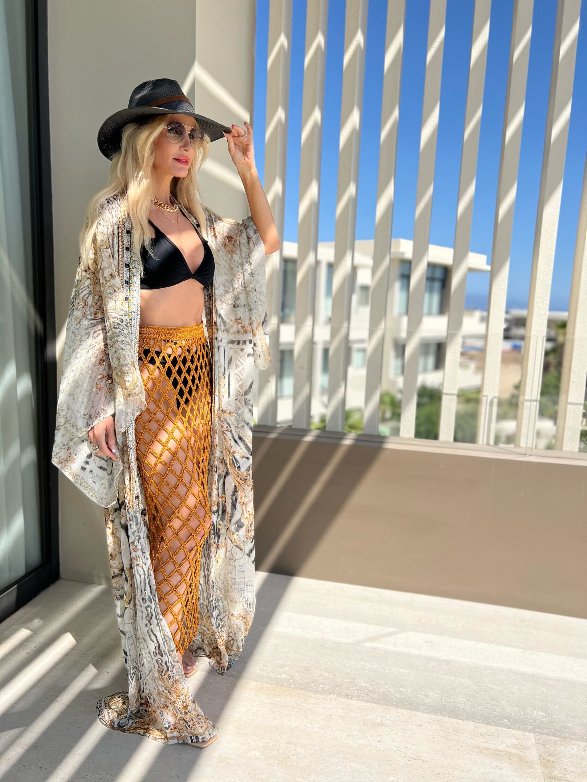 woman over 40 wearing black bikini white crochet cover up, kimono and black straw hat in chic vacation look