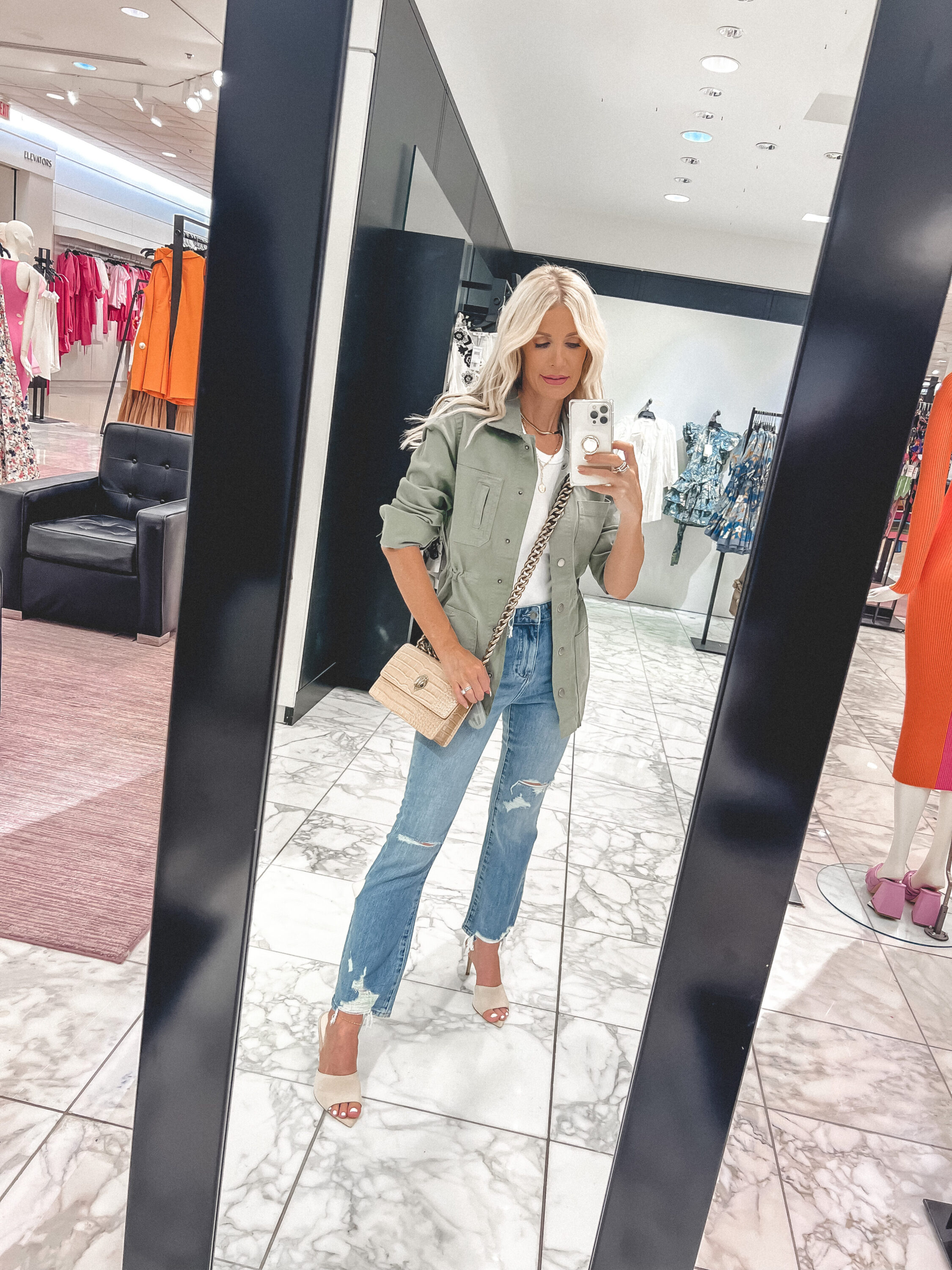 Dallas woman over 40 wearing pistola distressed light wash jeans with white bodysuit and green utility jacket.