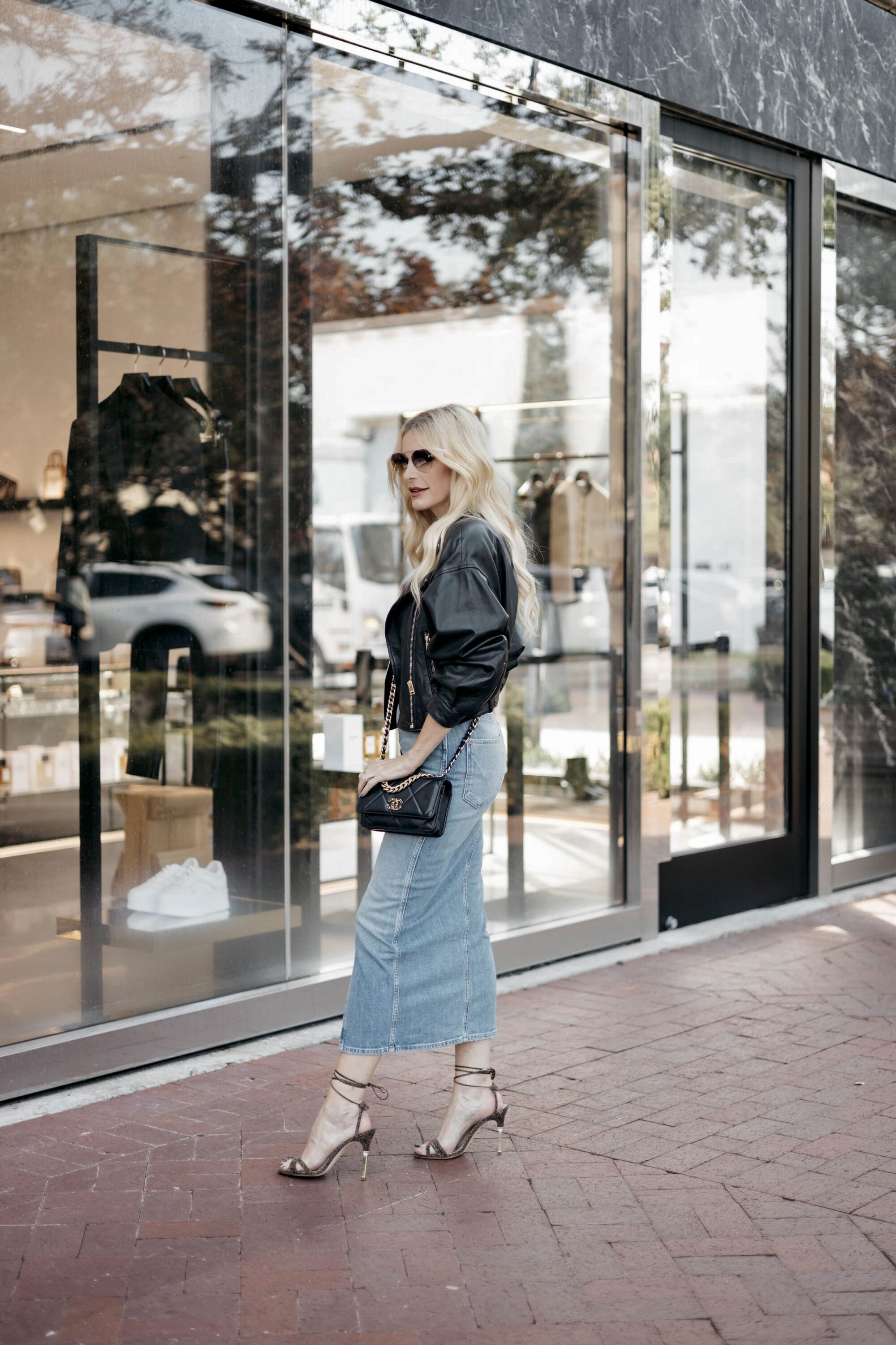 Over 40 fashion blogger wearing denim midi skirt with black leather jacket and snakeskin lace up heels.