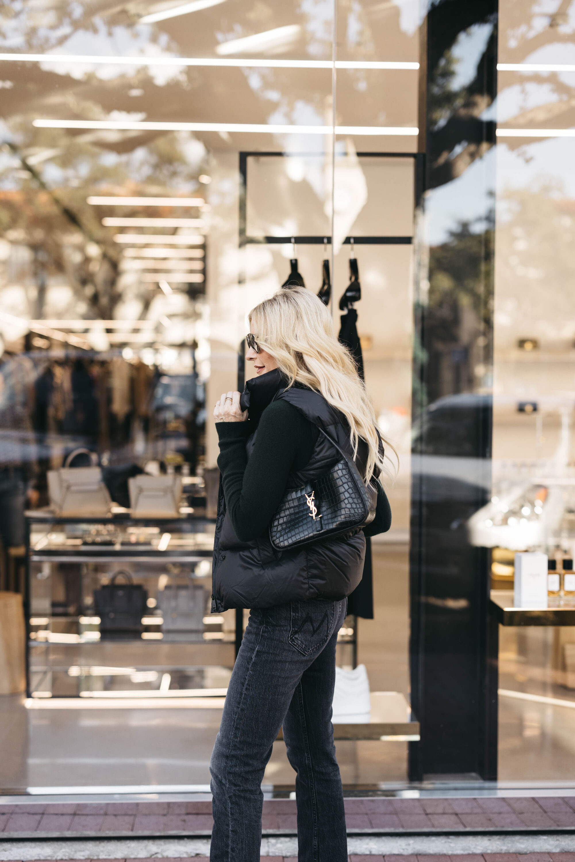woman over 40 wearing black jeans with black bodysuit and black puffer vest.