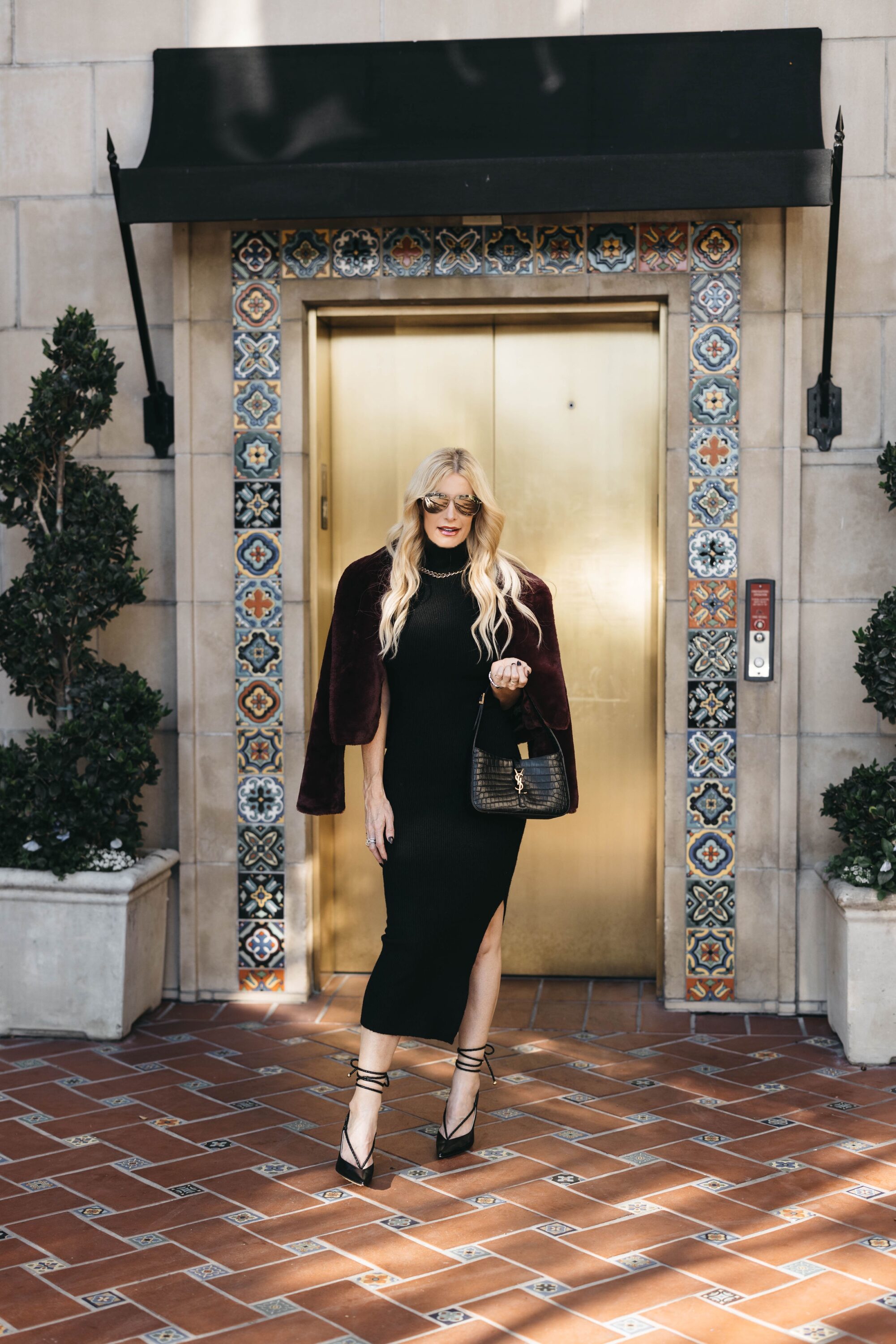 Over 40 fashion blogger wearing lace up heels with black sweater dress and faux fur jacket as an option for what to wear on New Year's Eve 2023.