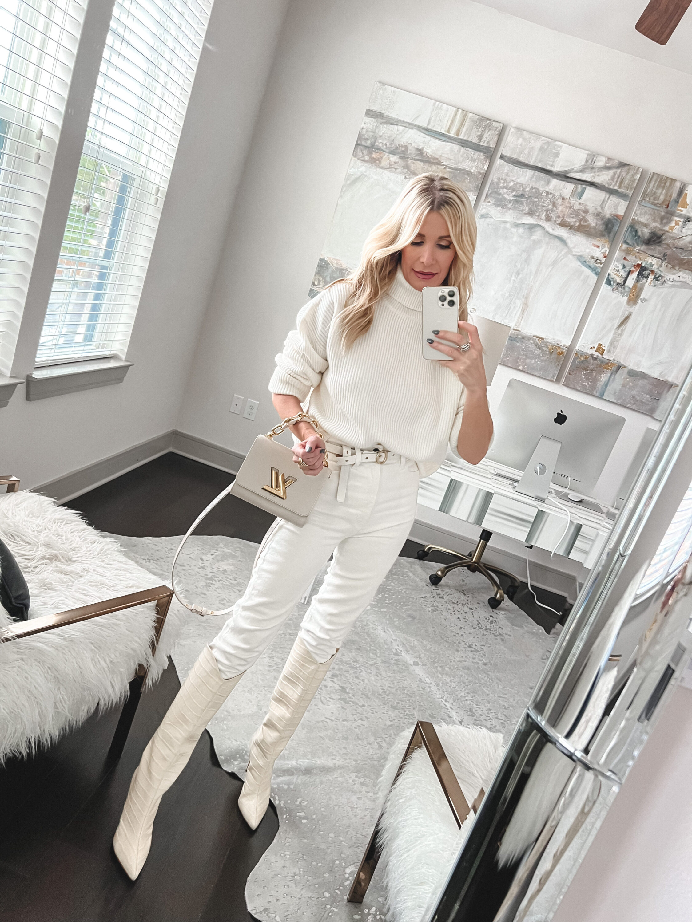 Over 40 woman wearing white turtleneck sweater with ivory leather pants and ivory boots.