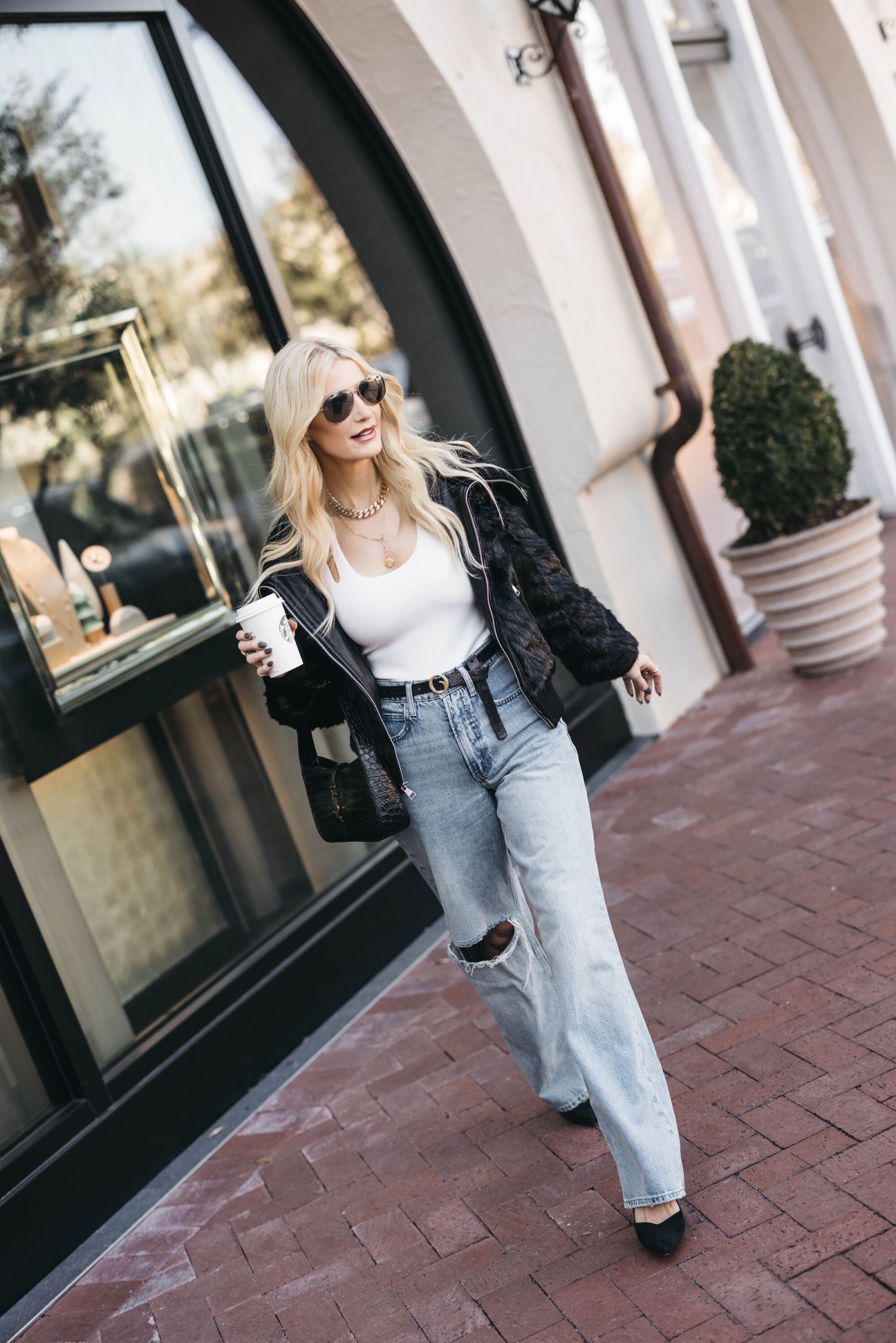Over 40 woman wearing black faux fur jacket with black belt, white bodysuit and baggy jeans all from Nordstrom.