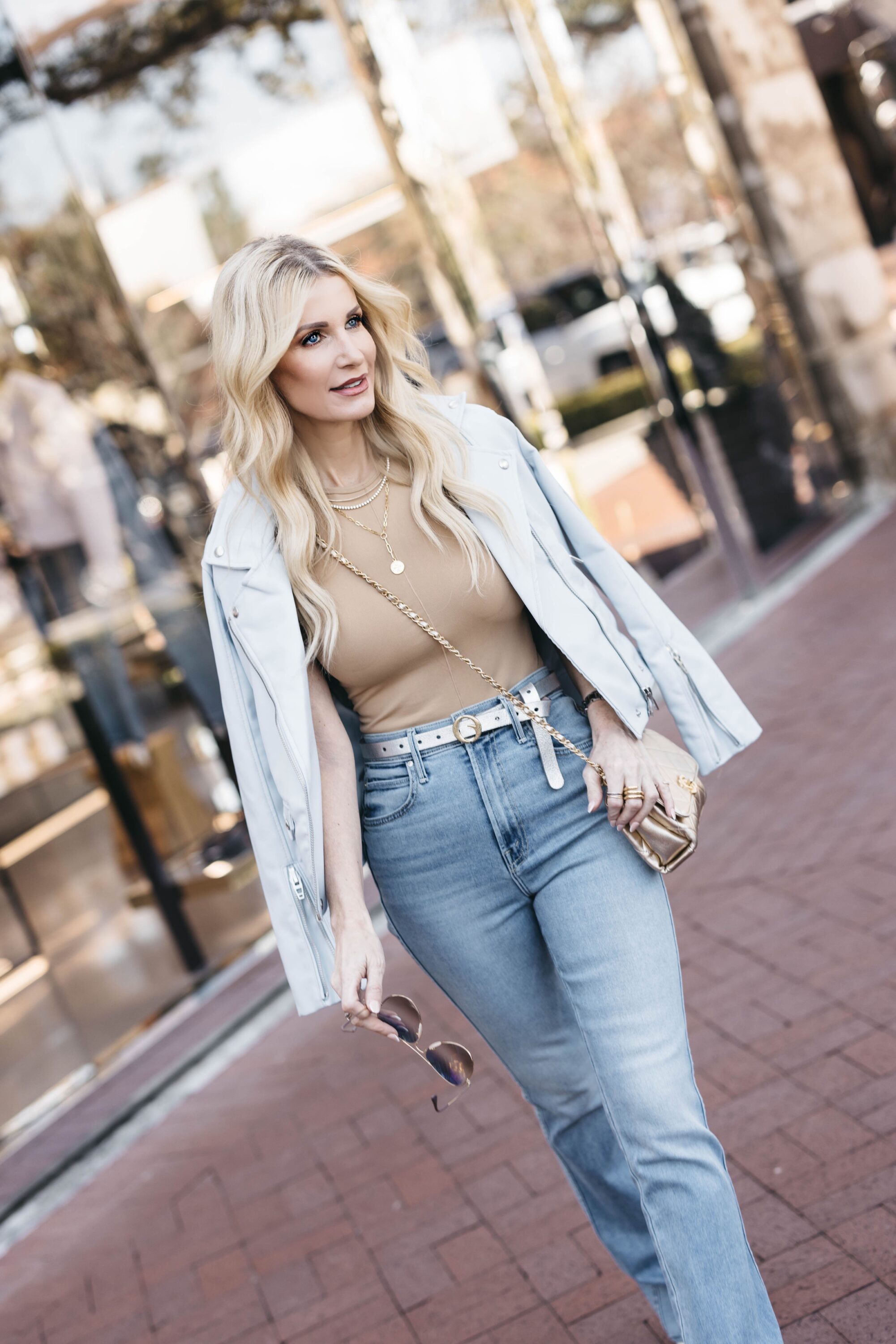 Fashion influencer over 40 wearing mother jeans with brown bodysuit and baby blue moto jacket as spring must-haves for 2023.