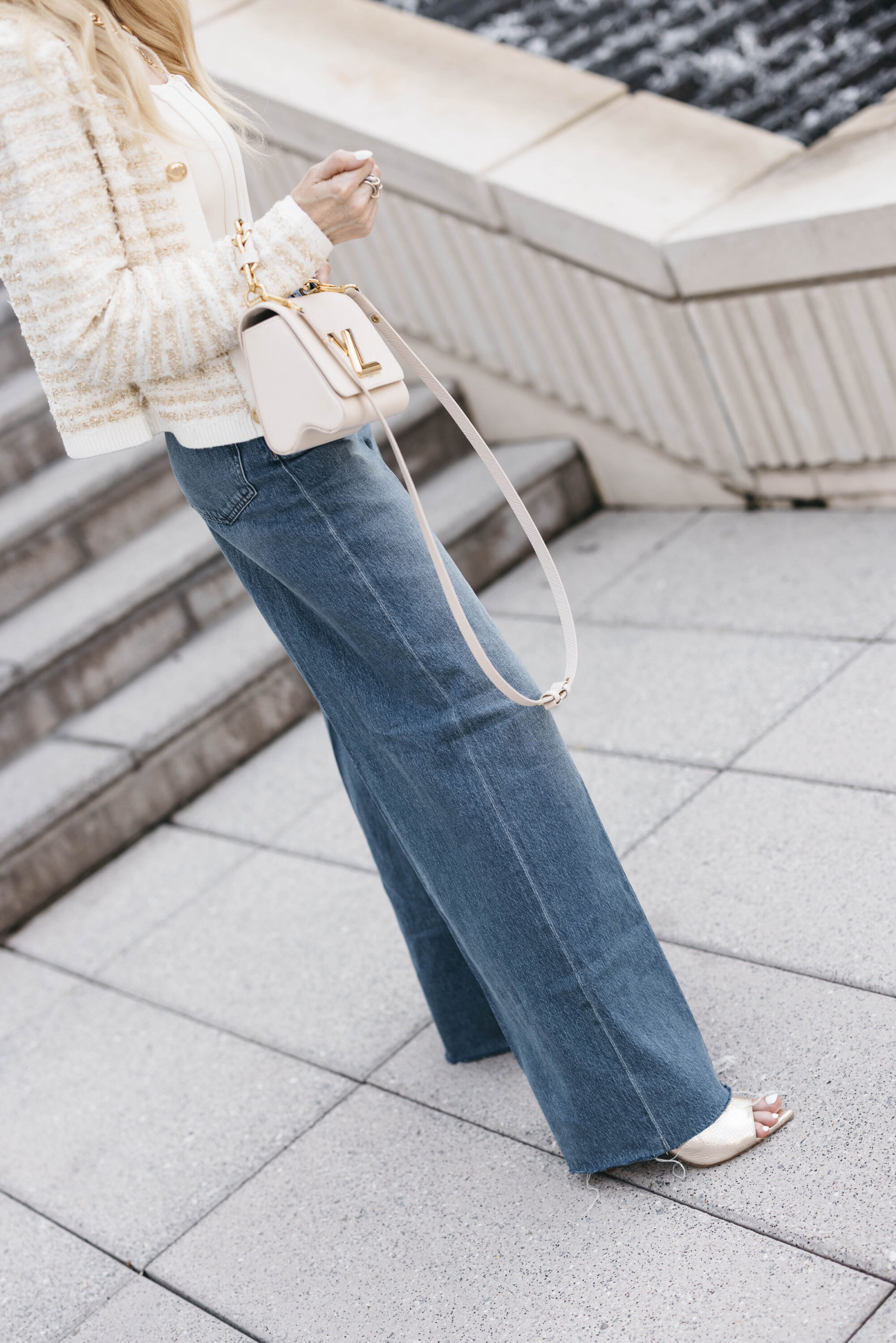 Dallas woman over 40 wearing wide leg jeans with sweater jacket and corset top with gold sandals.