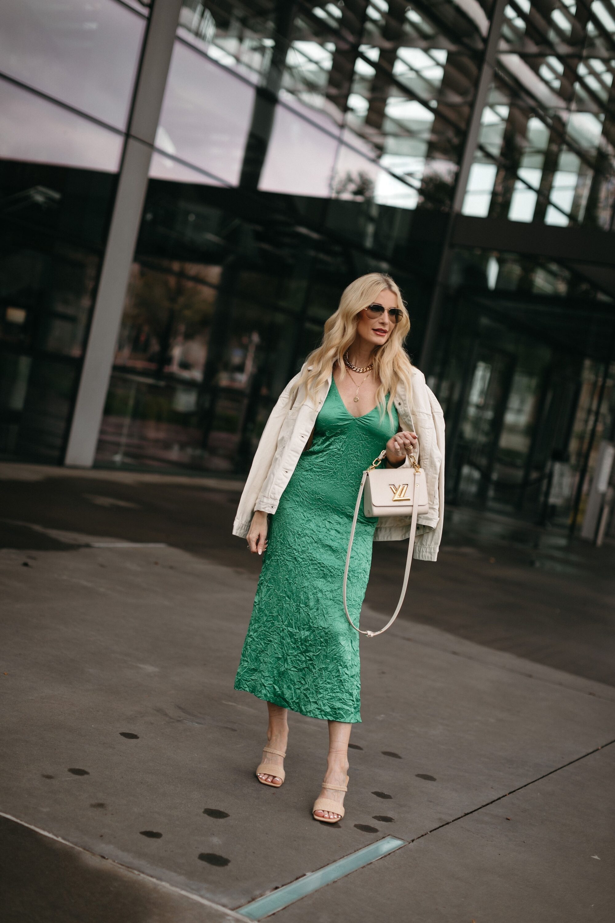 Over 40 fashion influencer wearing green crinkle dress with white leather jacket as one of 3 best spring dresses.