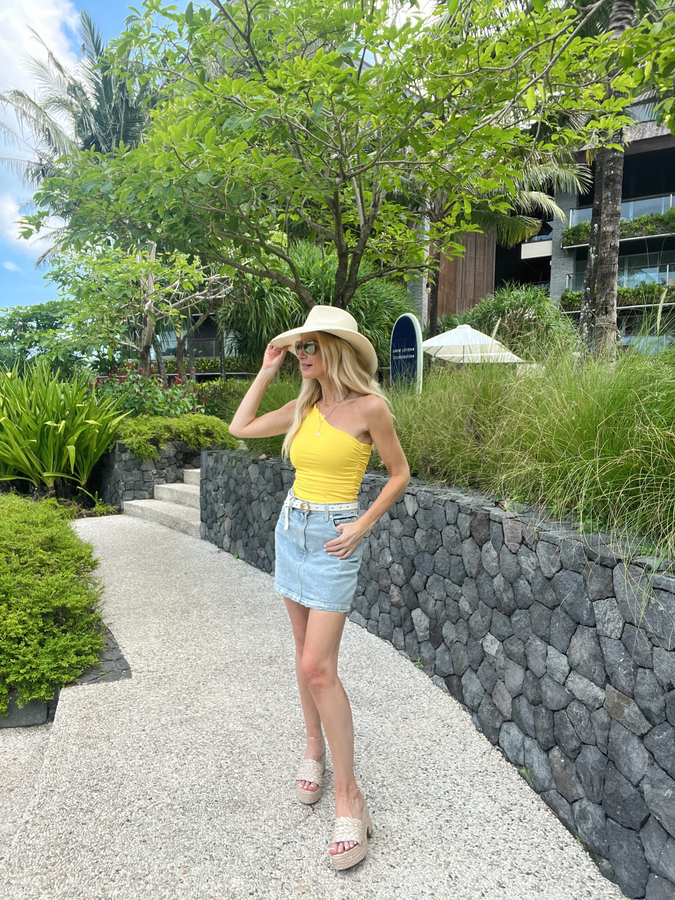 Dallas woman on a trip to Bali wearing an under $100 yellow summer top and a denim skirt with wedge platforms.