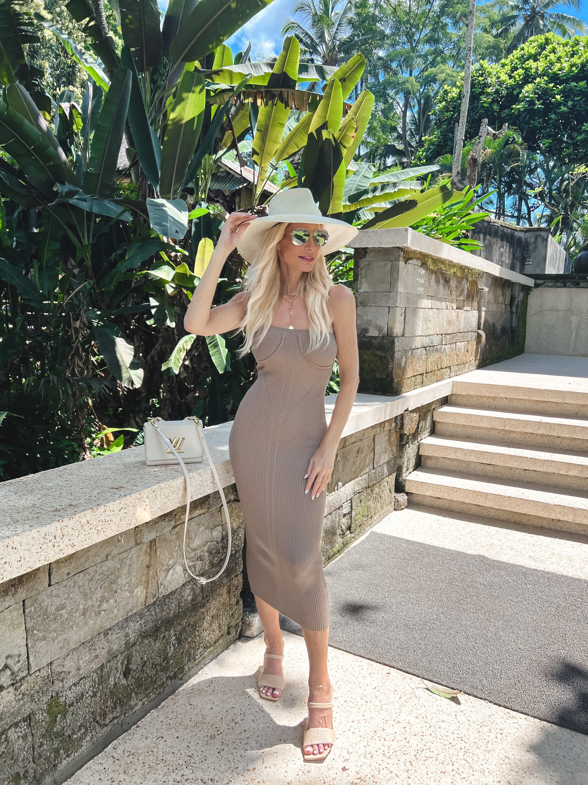 Over 40 fashion influencer wearing a strapless midi dress with heeled sandals and a sunhat.
