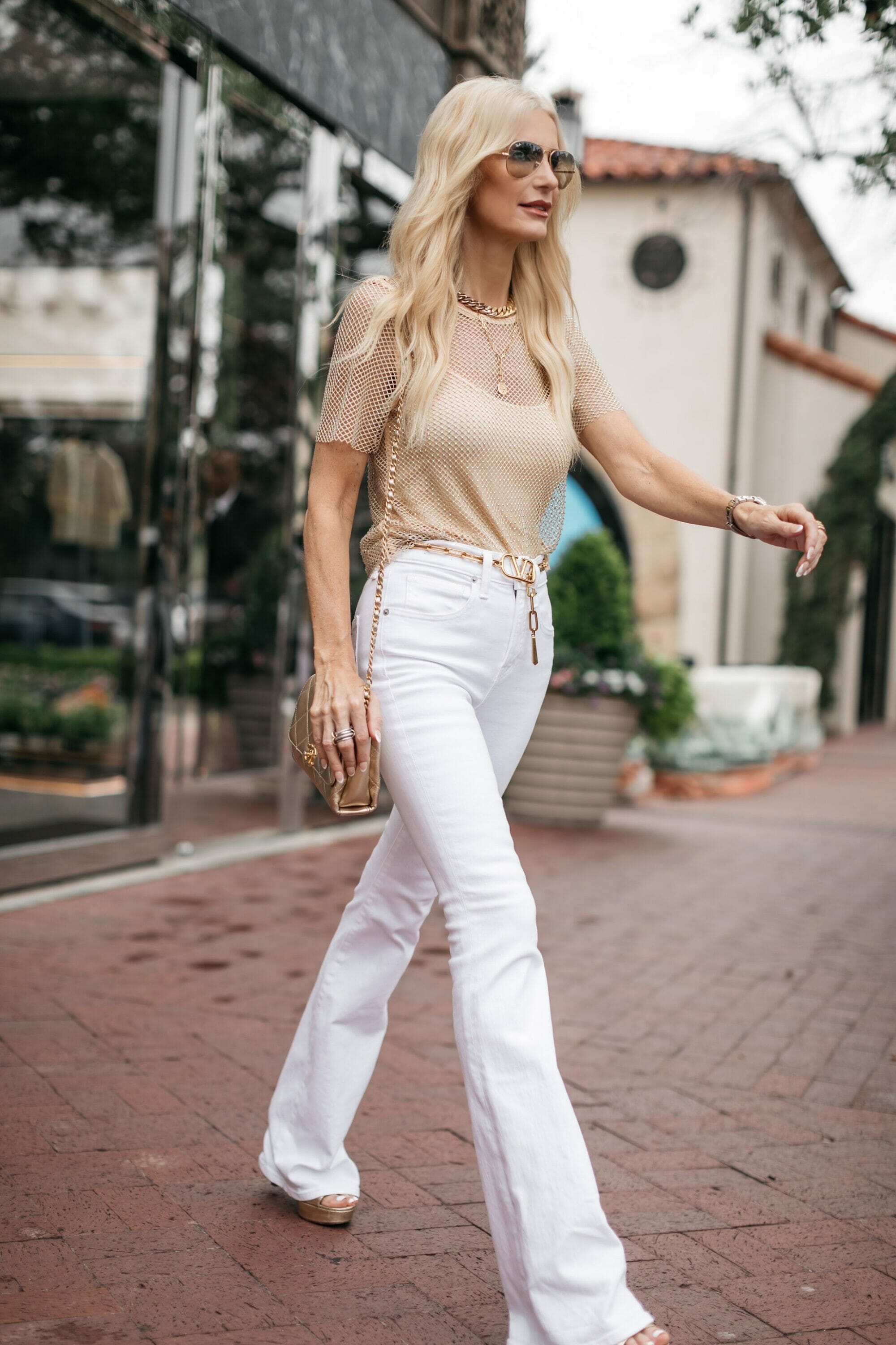 Over 40 woman from Dallas walks down the street with white jeans and a sequin top with gold accessories.