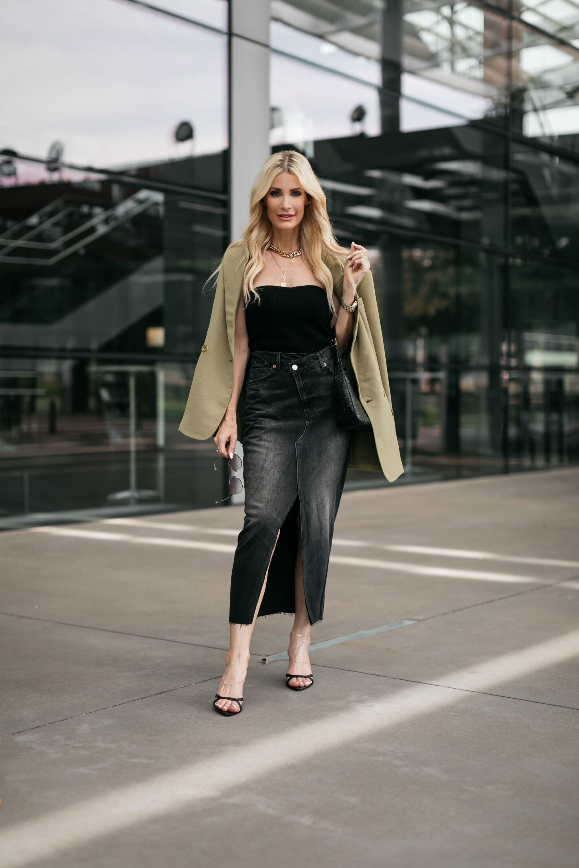 Dallas fashion influencer over 40 wears a black denim midi skirt with a black top and oversized blazer as an example of how to style a denim midi skirt.