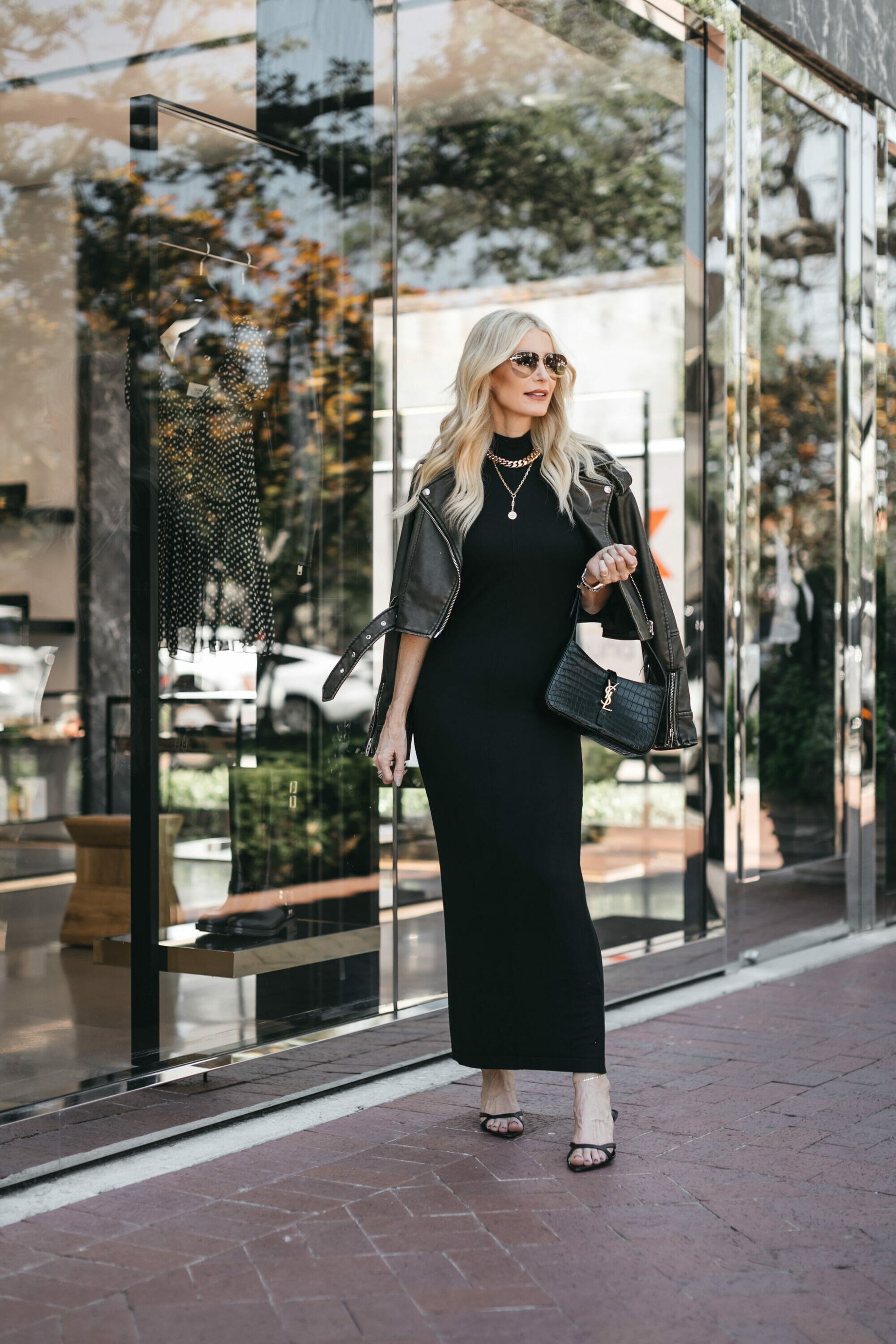 Dallas woman over 40 wearing black maxi dress with olive green leather jacket and black heels.