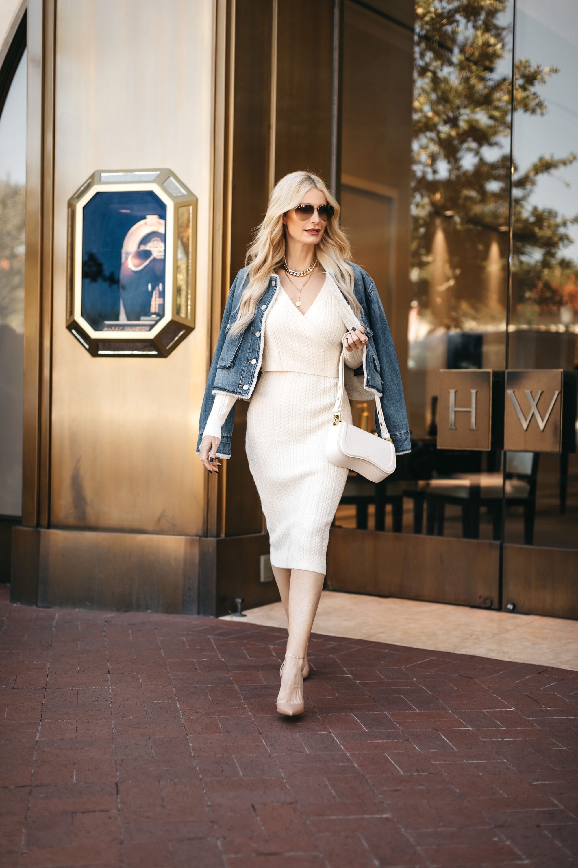 Dallas fashion icon wearing an ivory dress with a shearling denim jacket and nude heels.