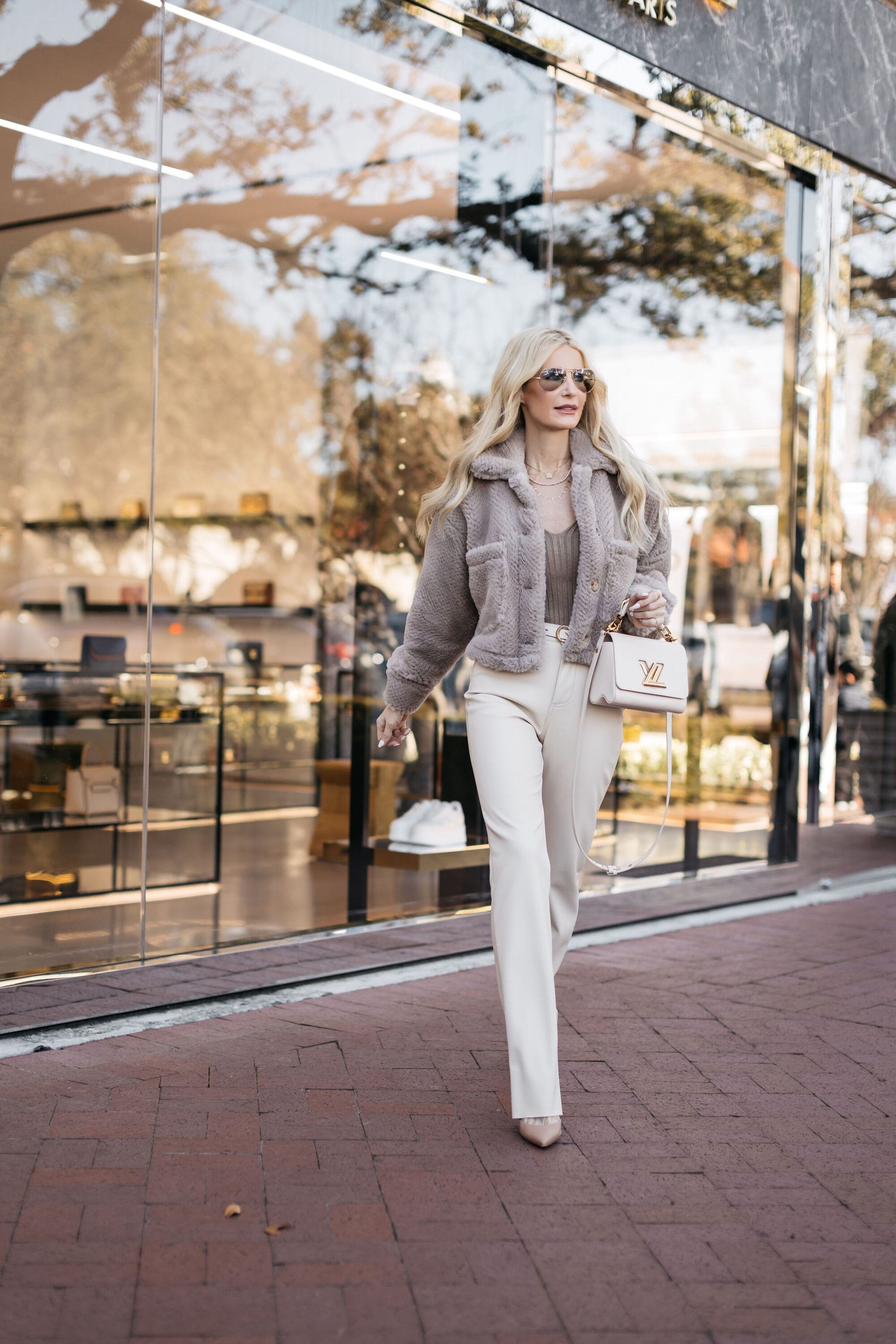 Dallas woman over 40 wearing a neutral teddy coat with ivory faux leather pants and nude heels.