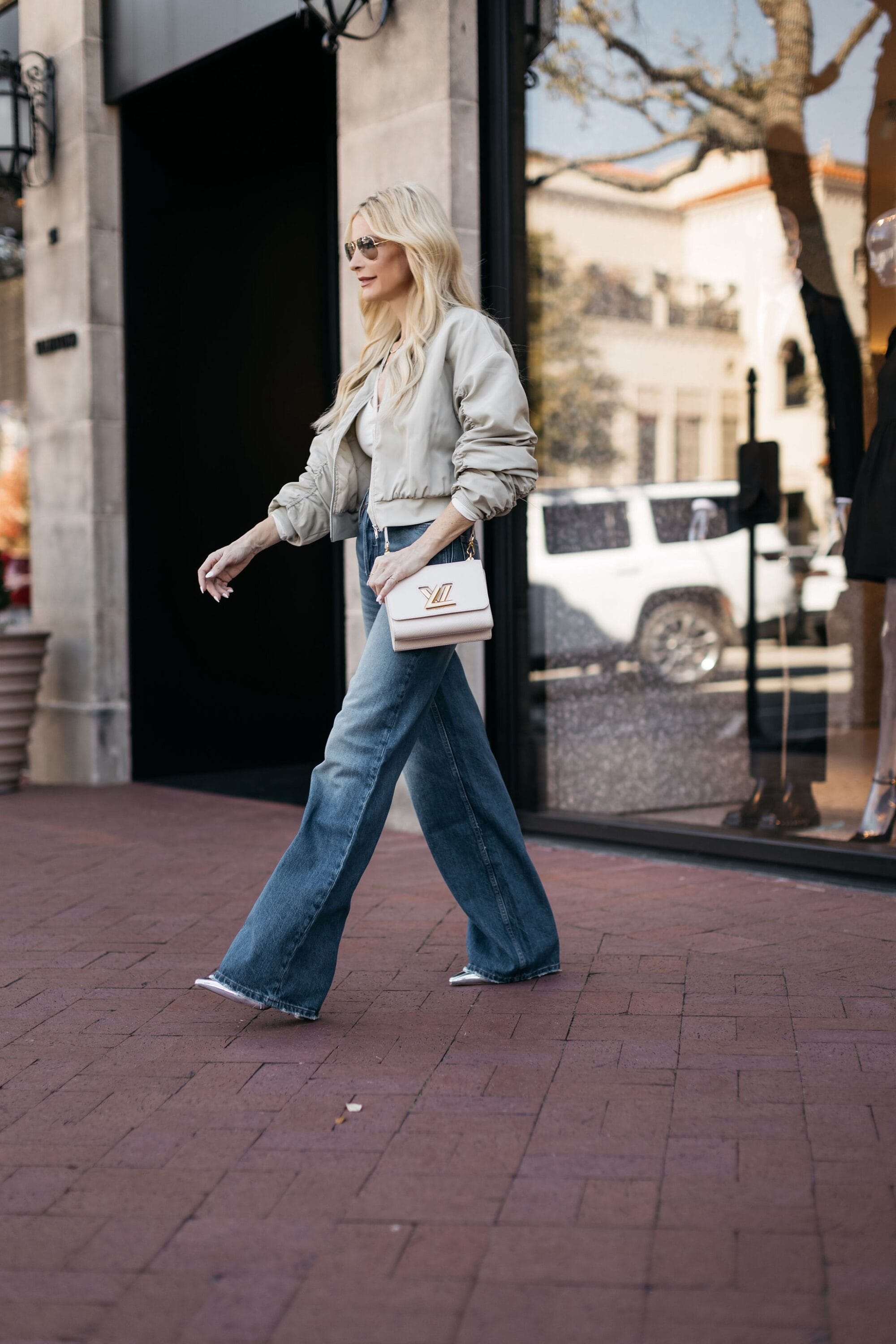 Over 40 Dallas fashion icon wearing wide leg jeans with a tan bomber jacket and silver heels.