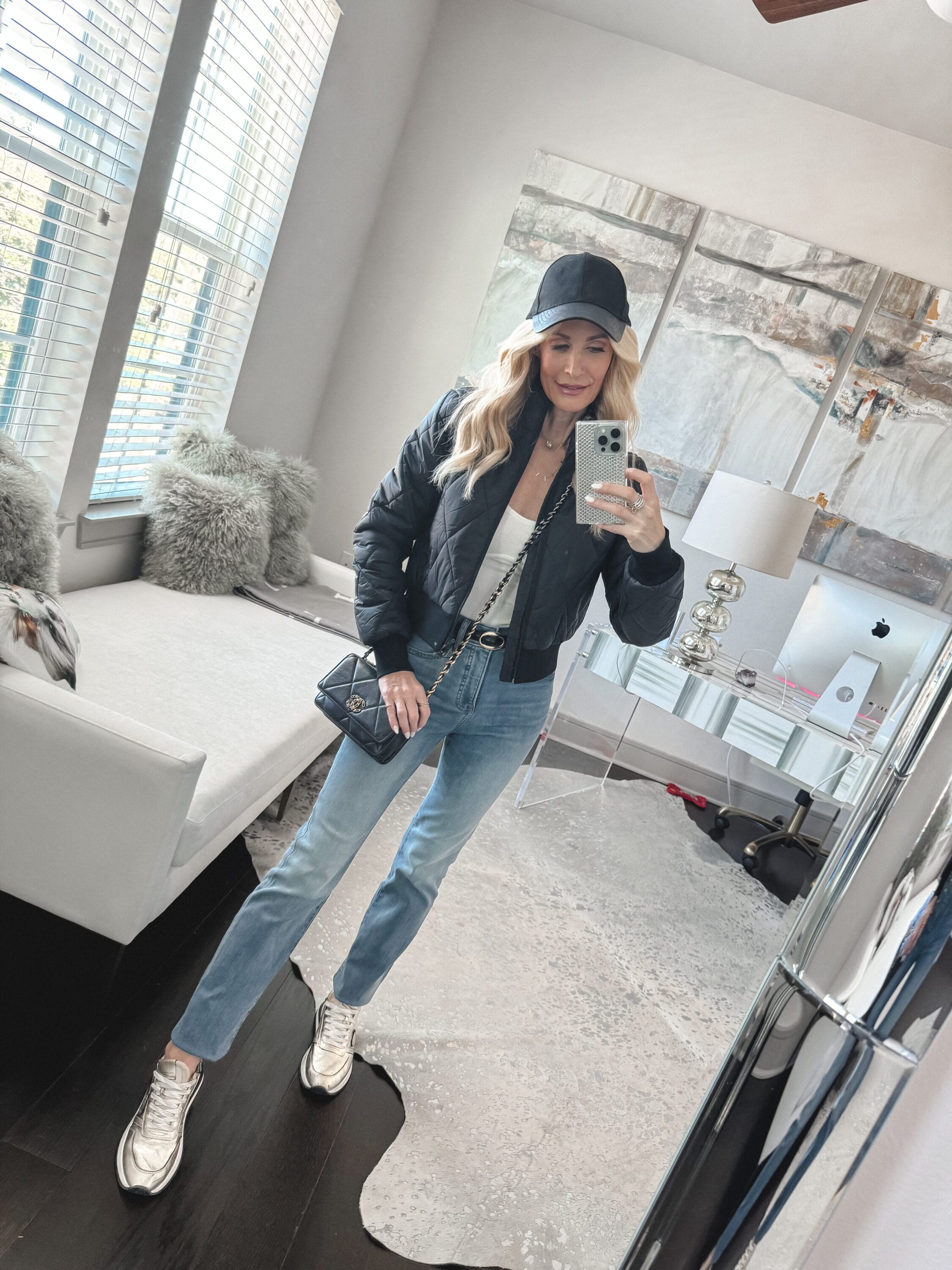 Over 40 fashion influencer from Dallas wearing straight leg jeans, a black quilted bomber jacket and black faux leather baseball cap as the last of 4 examples of how to style sneakers.