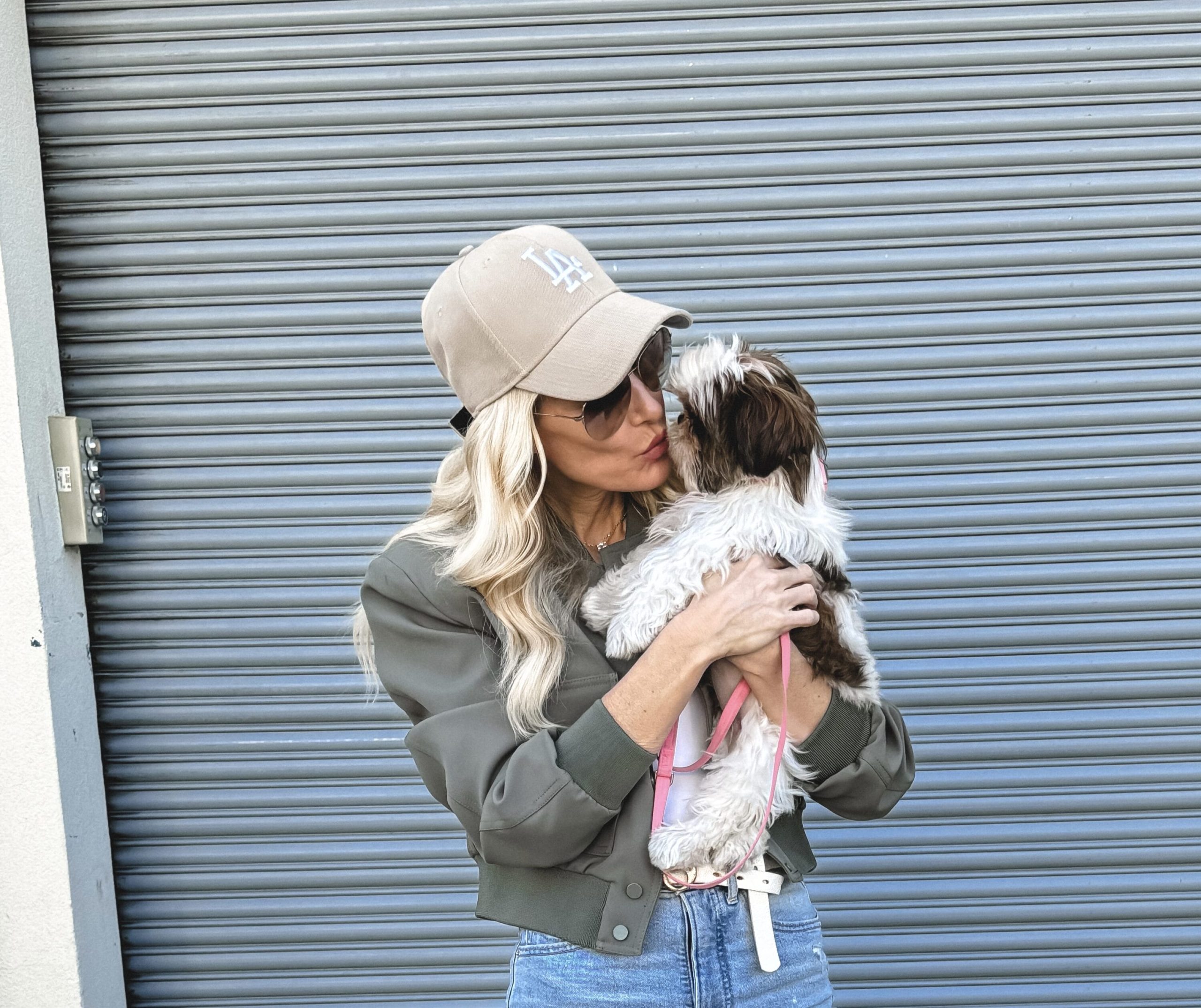 Dallas fashion influencer for women over 40 wearing a sage green bomber jacket with a white bodysuit and skinny jeans with a beige LA hat as one of 4 examples of how to style sneakers.
