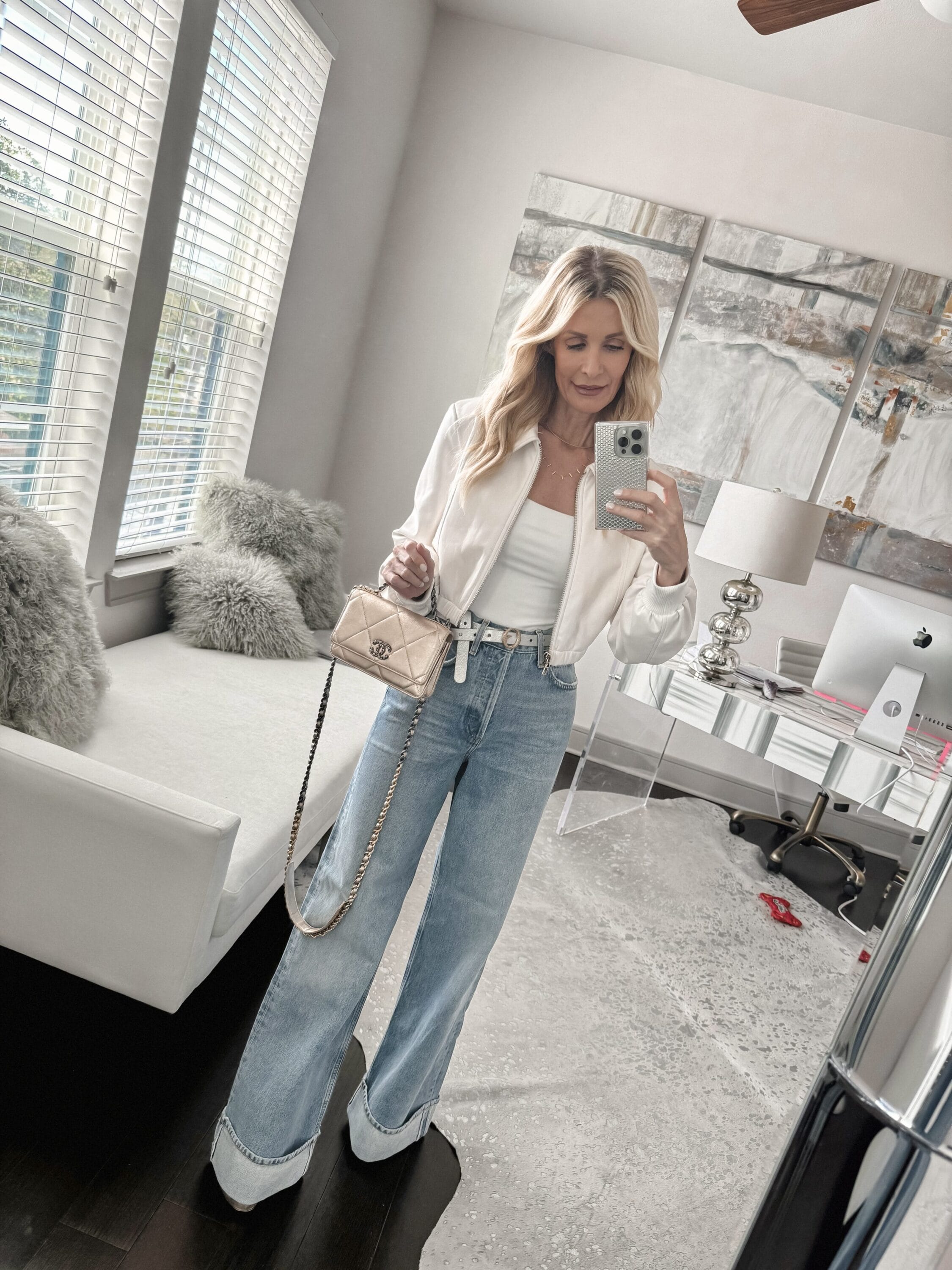 Dallas fashion influencer over 40 wearing cuffed jeans from Frame with a cream collarless jacket and gold platform heels with a gold hand bag.