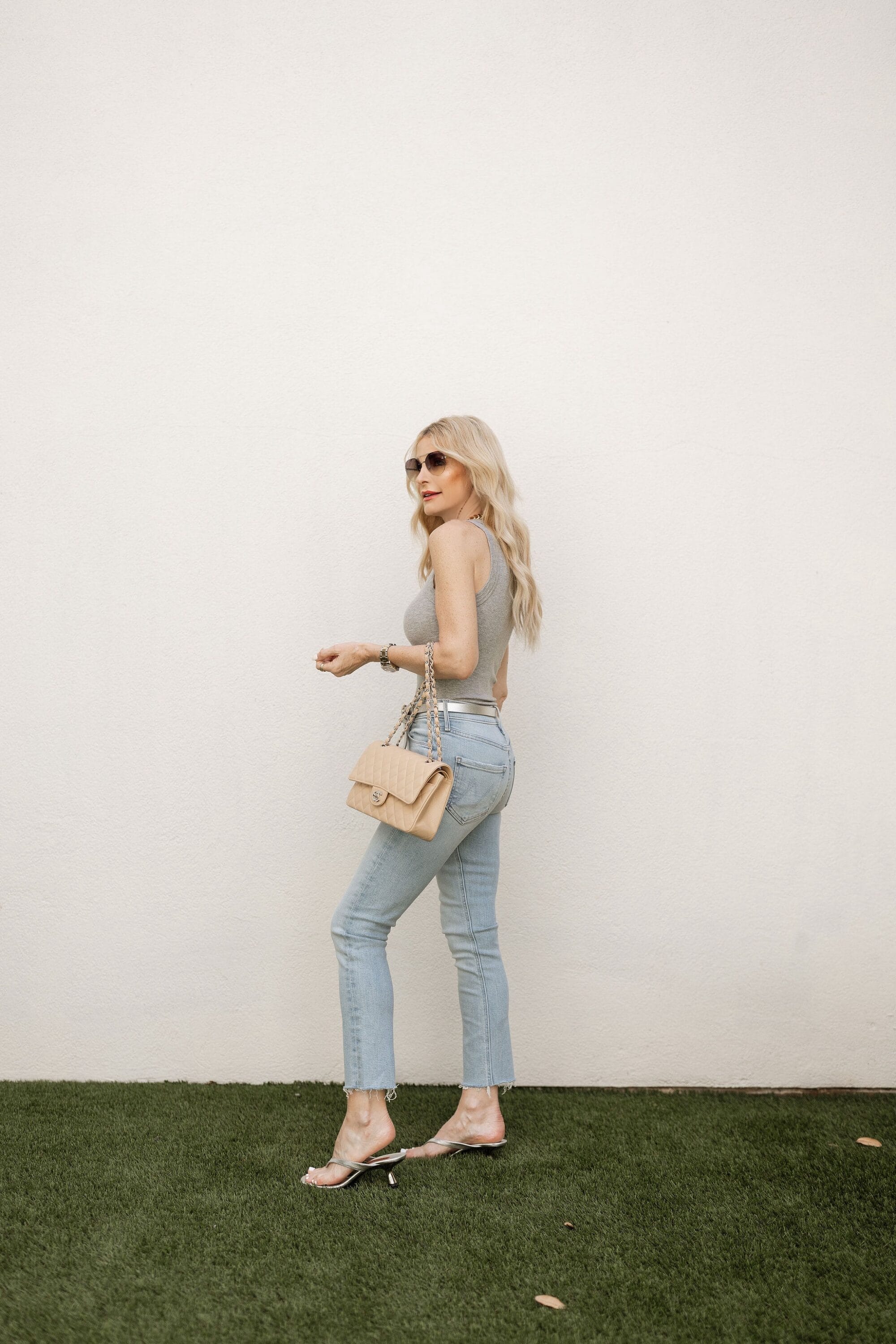 Over 40 fashion influencer wearing a pair of silver kitten heels with a grey ruched tank and straight leg jeans.