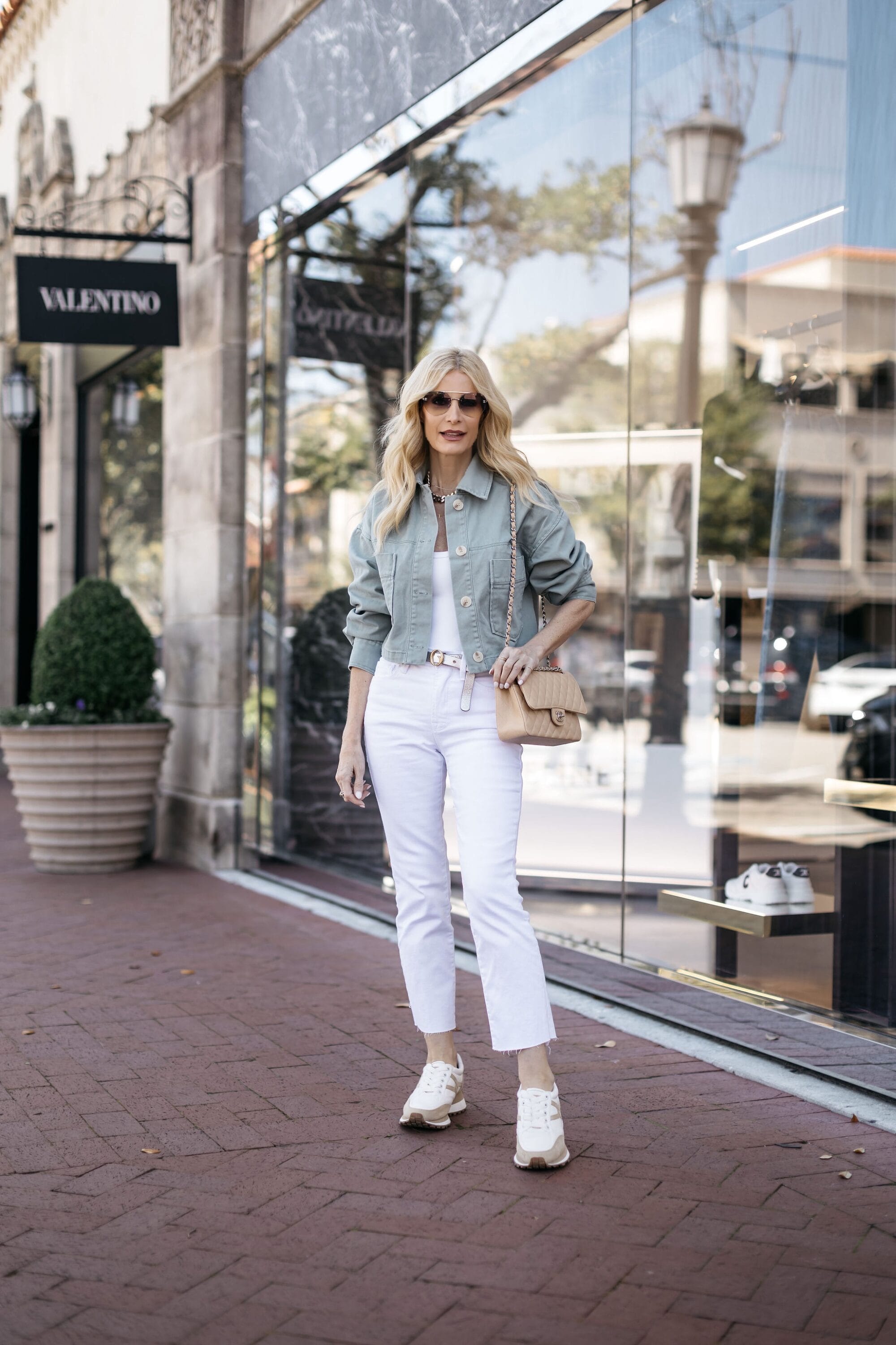 Dallas fashion icon wearing the IT pair of white jeans for spring 2024 with a green utility jacket and neutral sneakers.
