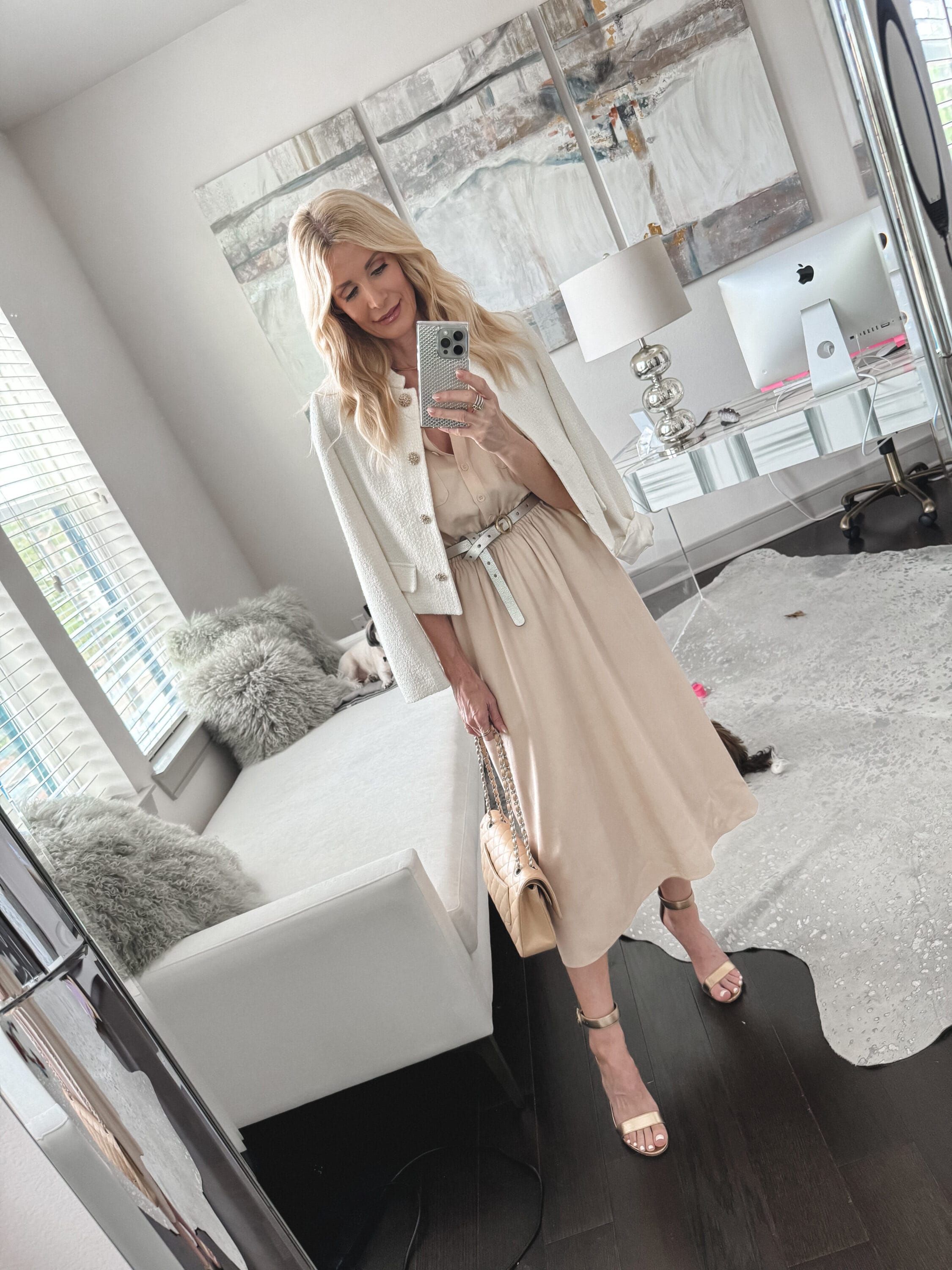 Woman over 40 wearing a being dress with an cropped ivory jacket and gold heels.