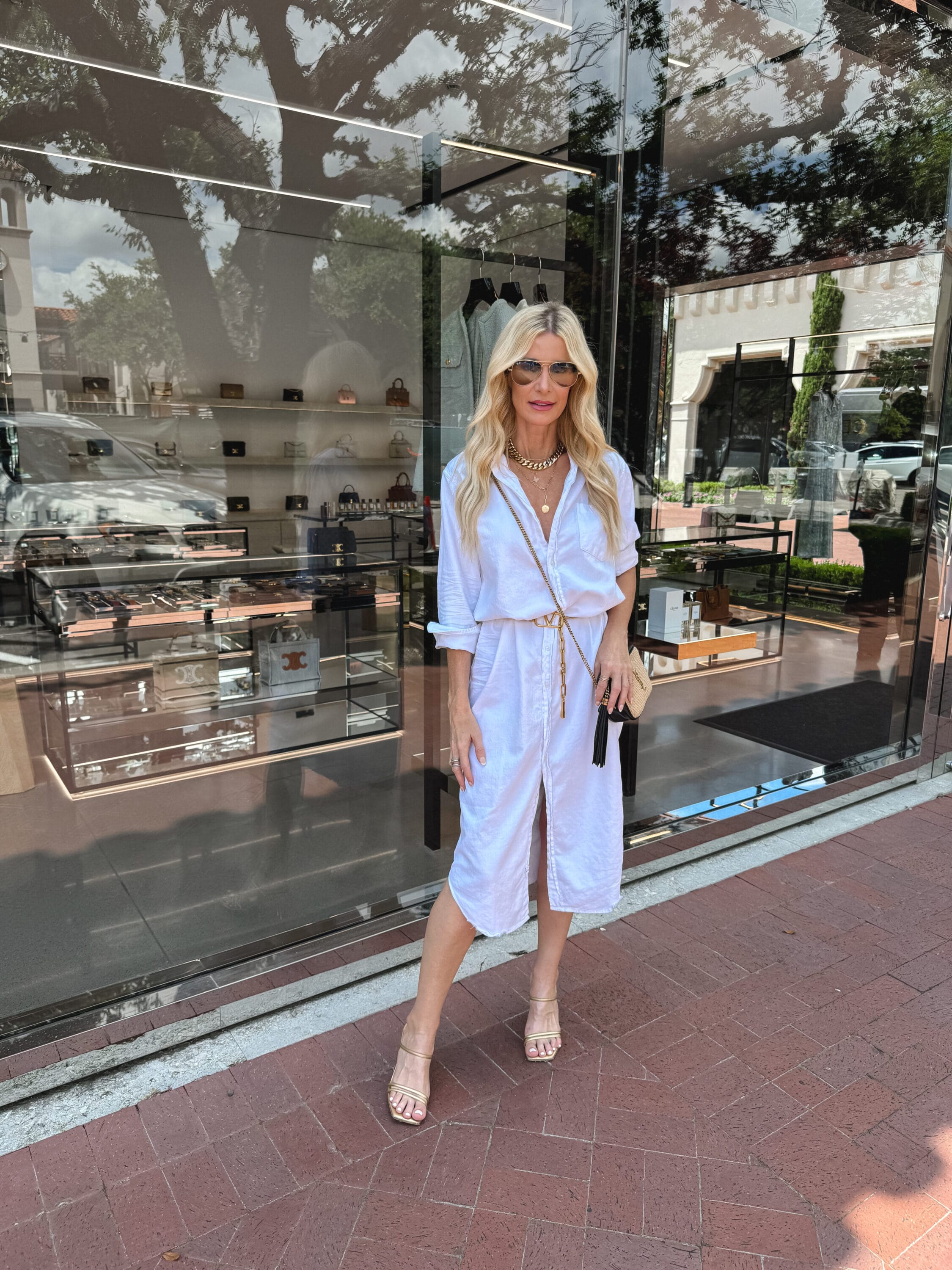 Over 40 fashion stylist from Dallas wearing an easy white shirt dress with gold heels and a designer handbag as one of 5 summer wardrobe essentials.