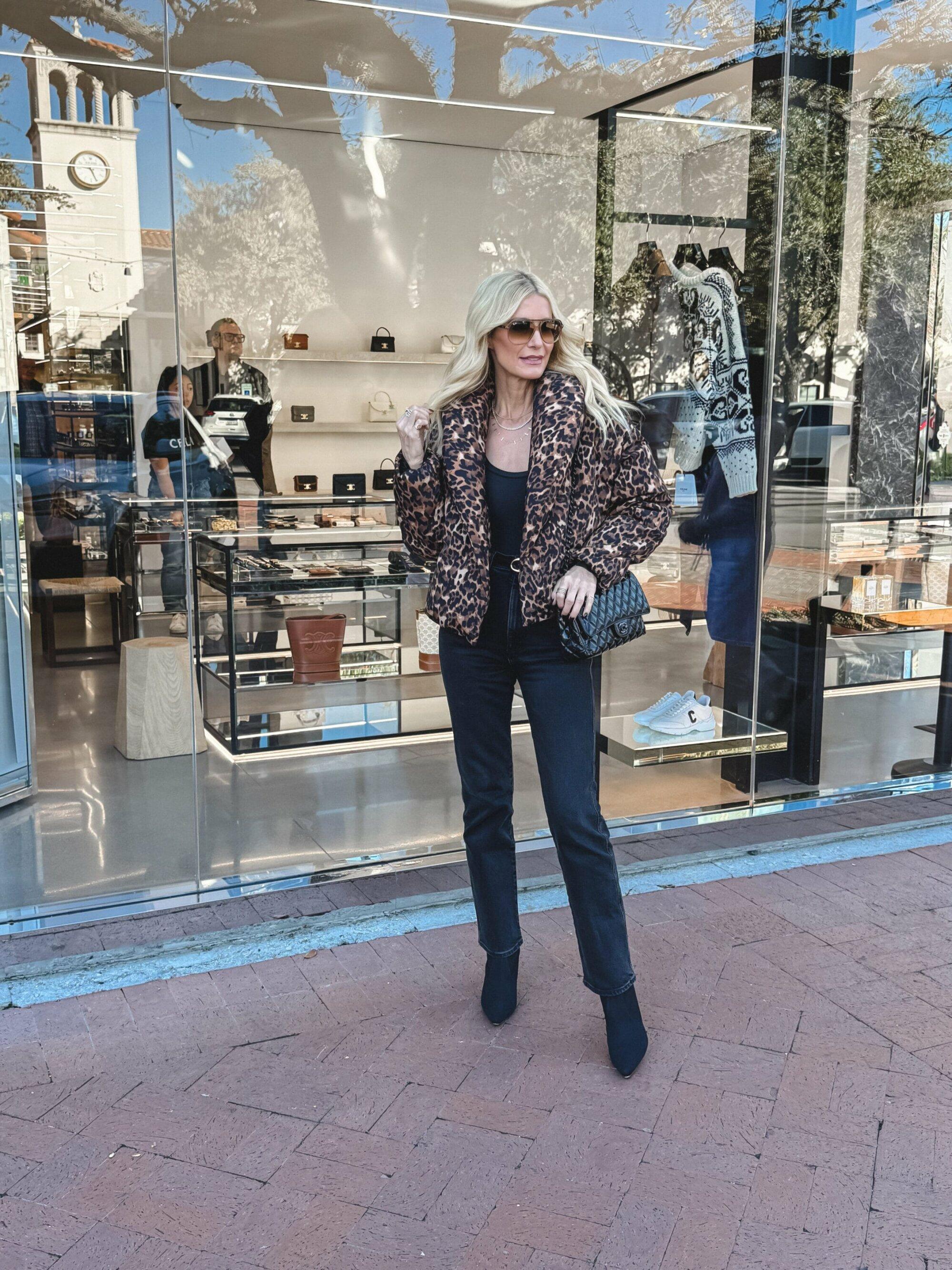 Dalla woman over 40 wearing a leopard print puffer jacket with black straight leg jeans and suede ankle booties as one of 2025's hottest denim trends.