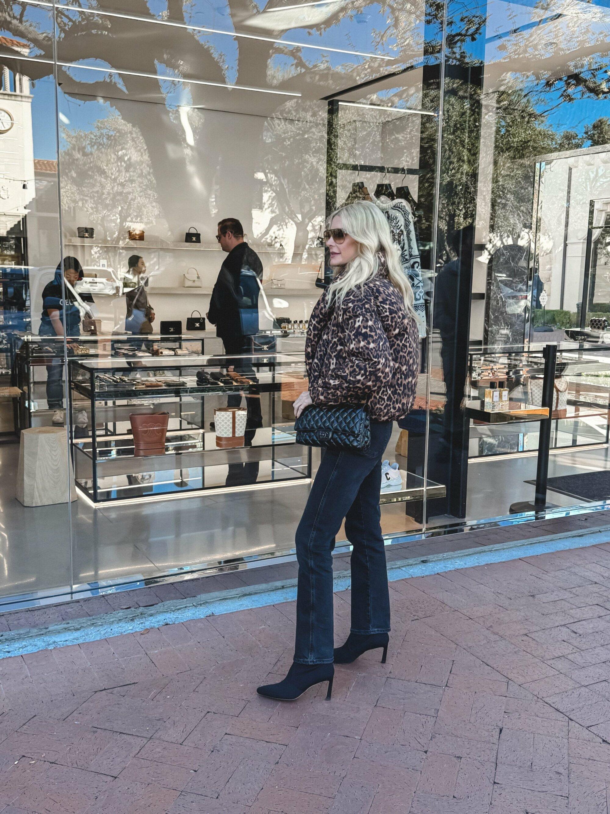 Dallas woman over 40 wearing a leopard puffer jacket with black wash straight leg jeans and suede ankle booties.