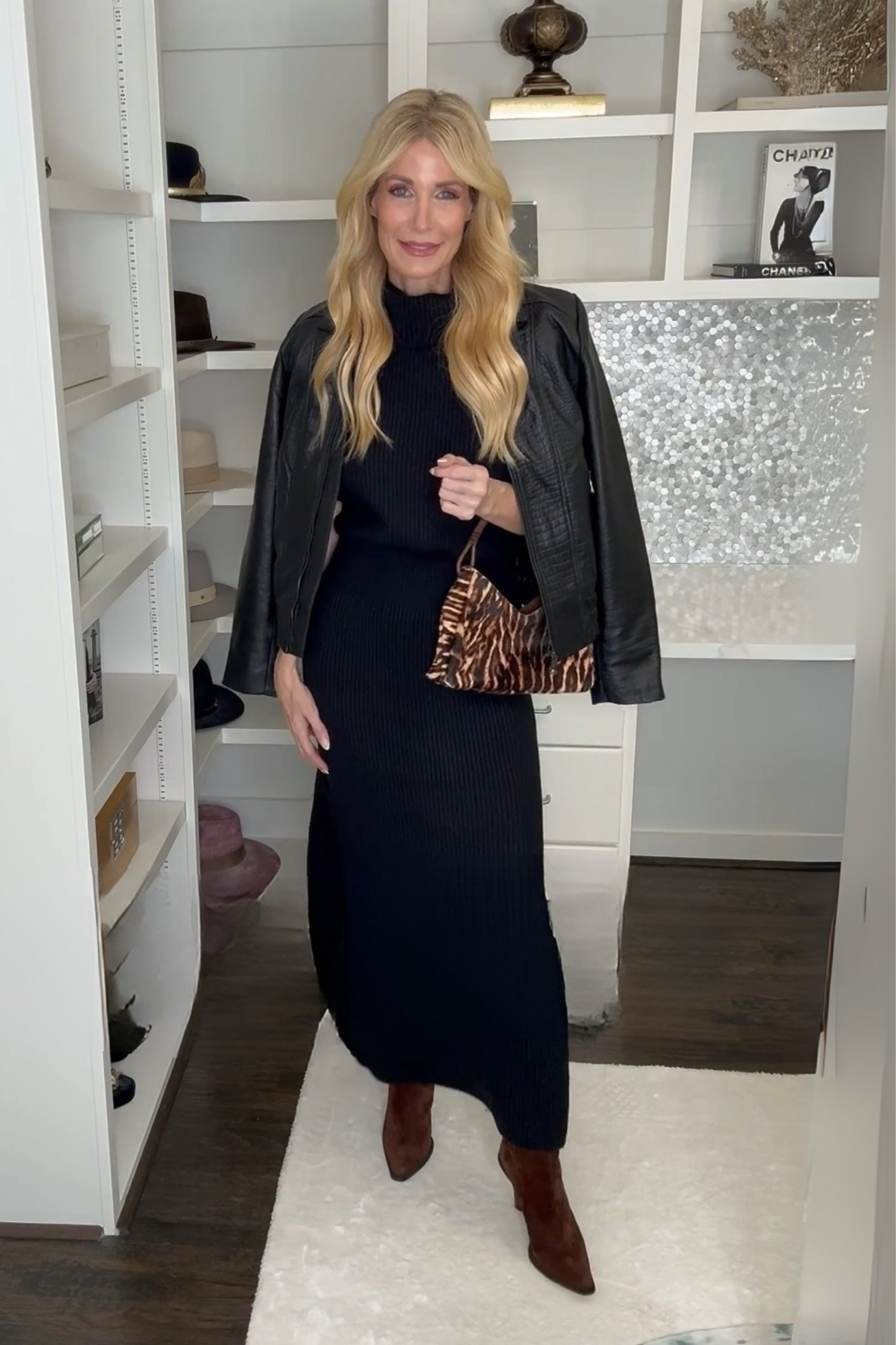 Over 40 fashion icon wearing a pair of chocolate brown knee high boots with a black sweater dress.