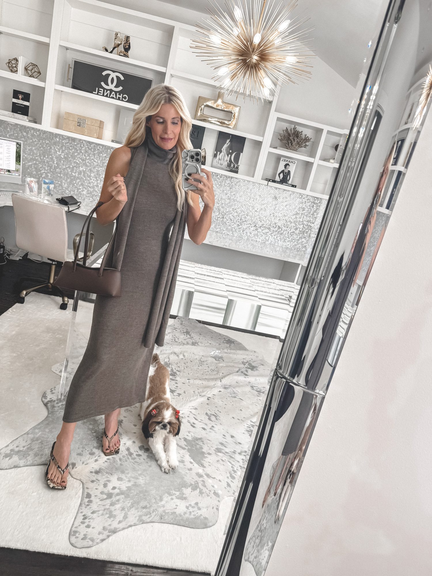 Over 40 fashion influencer wearing a sleeveless taupe knit midi dress with a matching scarf in her home office, holding a brown east west handbag.