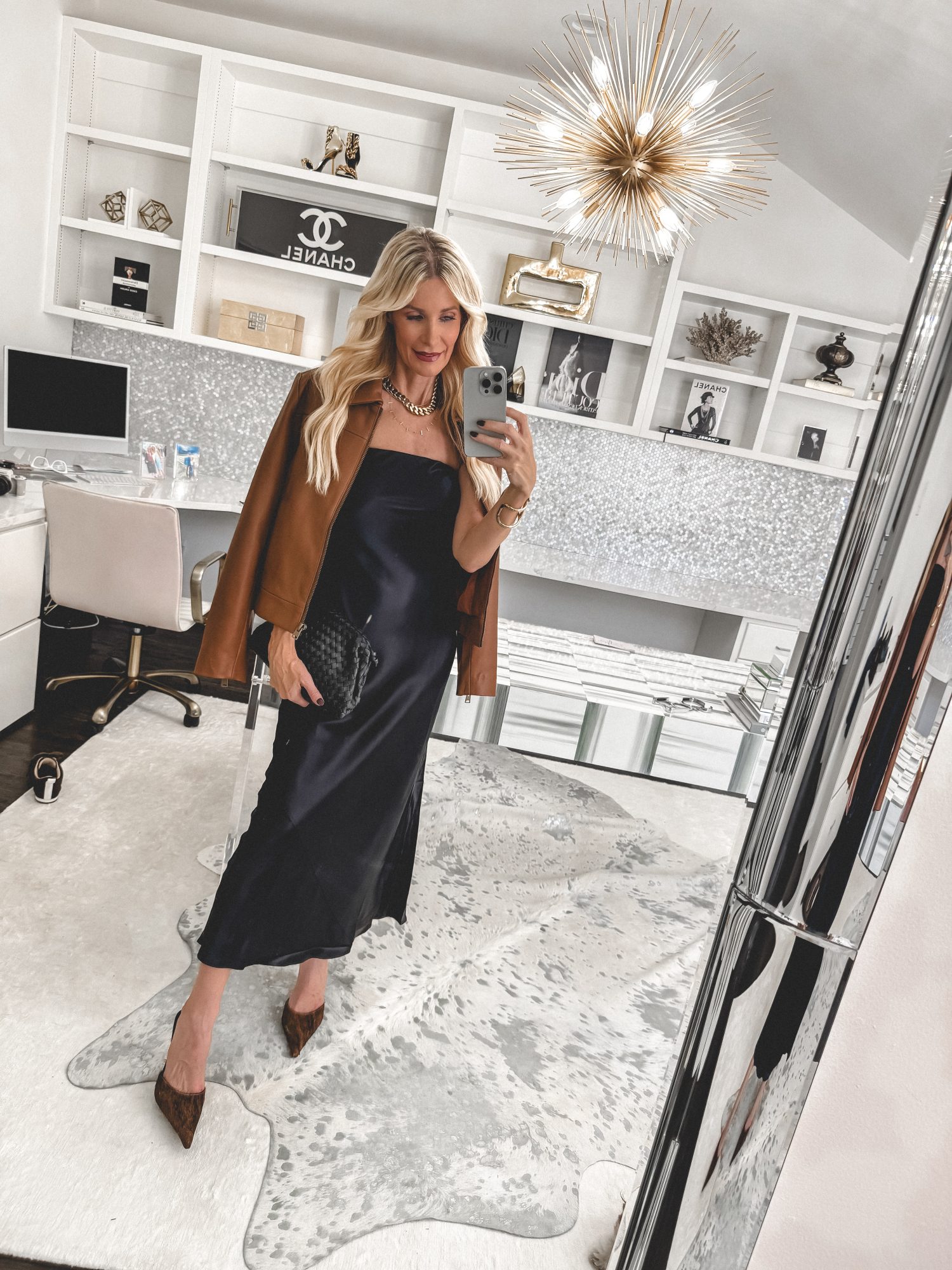 Over 40 fashion stylist wearing a leather bomber jacket with a sleek silk maxi dress and calf hair heels.