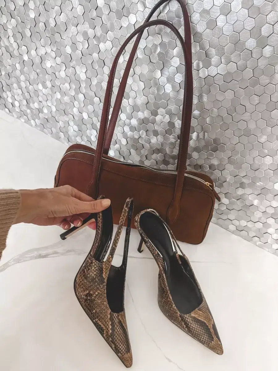 Flat lay image of snakeskin heels and a brown zip top handbag.
