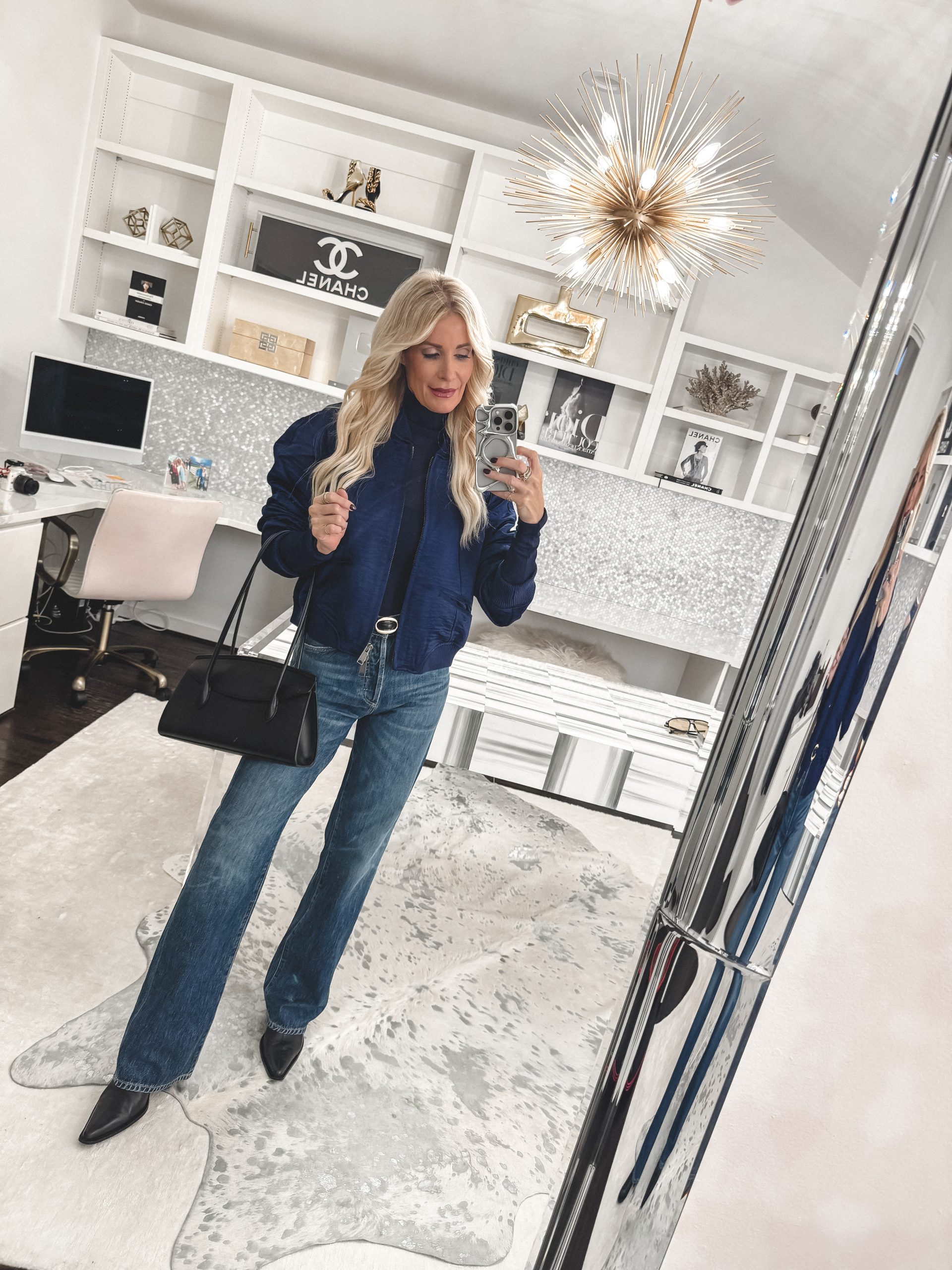 Over 40 fashion blogger wearing a navy satin bomber jacket with blue jeans and black leather boots.