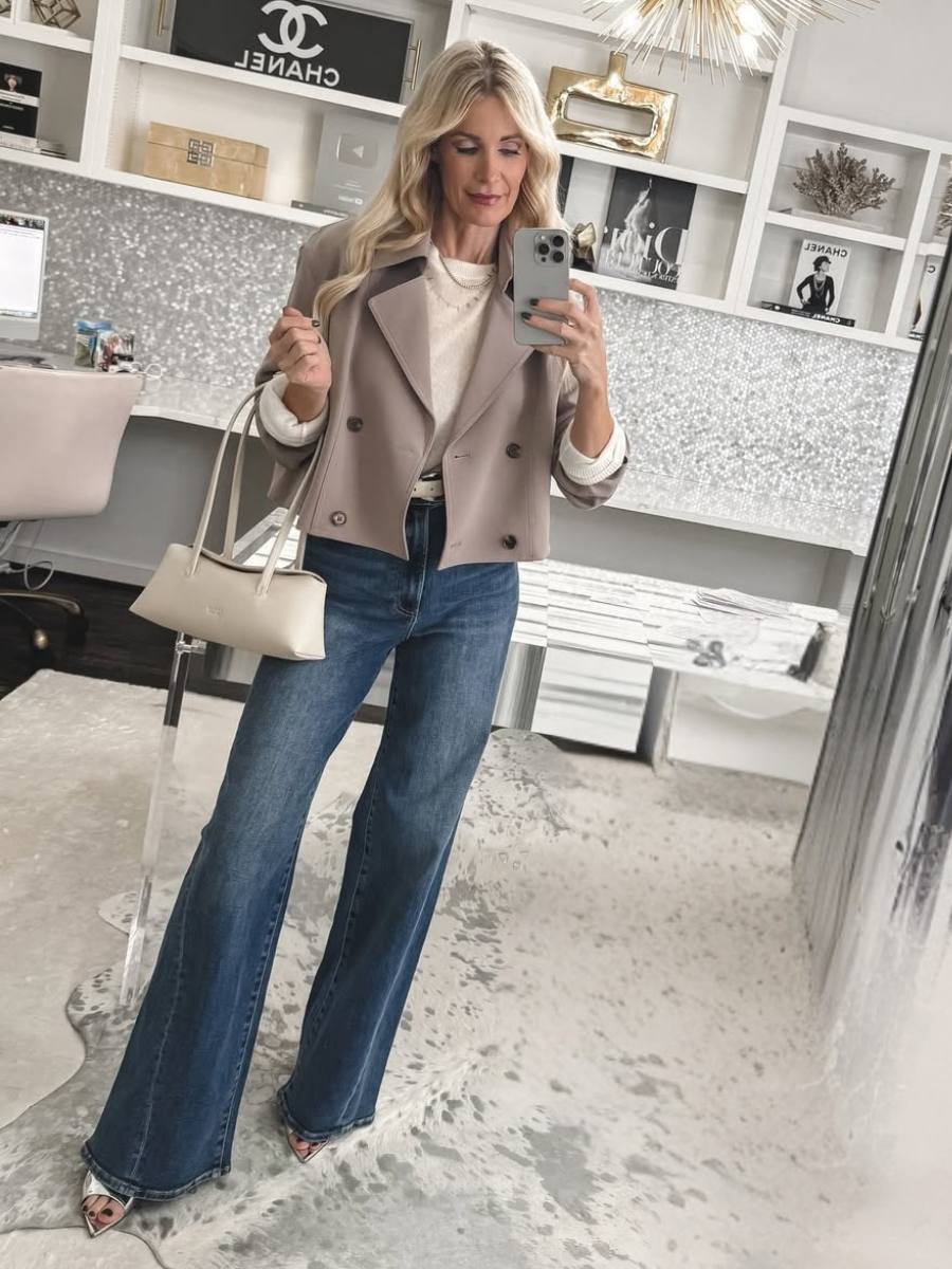 Over 40 fashion blogger wearing a cropped trench coat with wide leg jeans, silver heels and an ivory handbag.