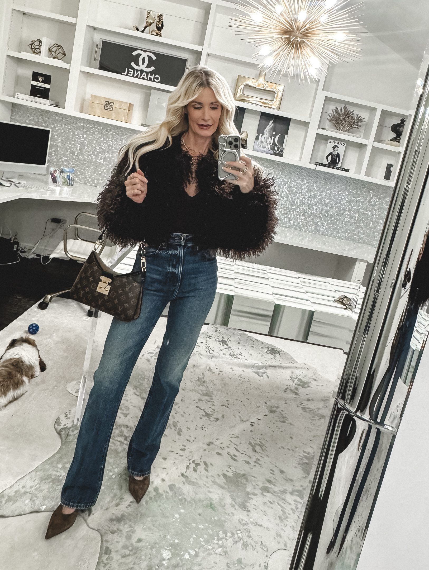 Over 40 woman wearing a faux fur jacket and cigarette jeans with a Louis Vuitton hand bag and leopard heels. 