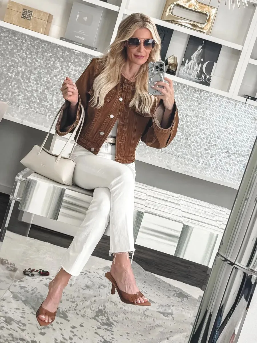 Over 40 fashion stylist wearing ivory denim with a brown denim jacket and clear heels.
