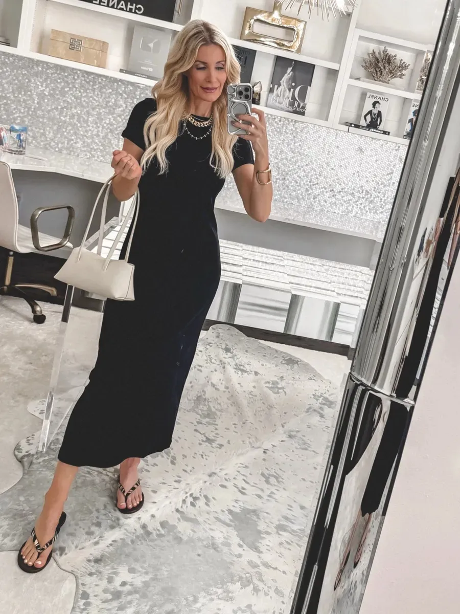 Over 40 fashion icon wearing zebra print flat sandals with a fitted black midi dress and white handbag for a stylish summer outfit.