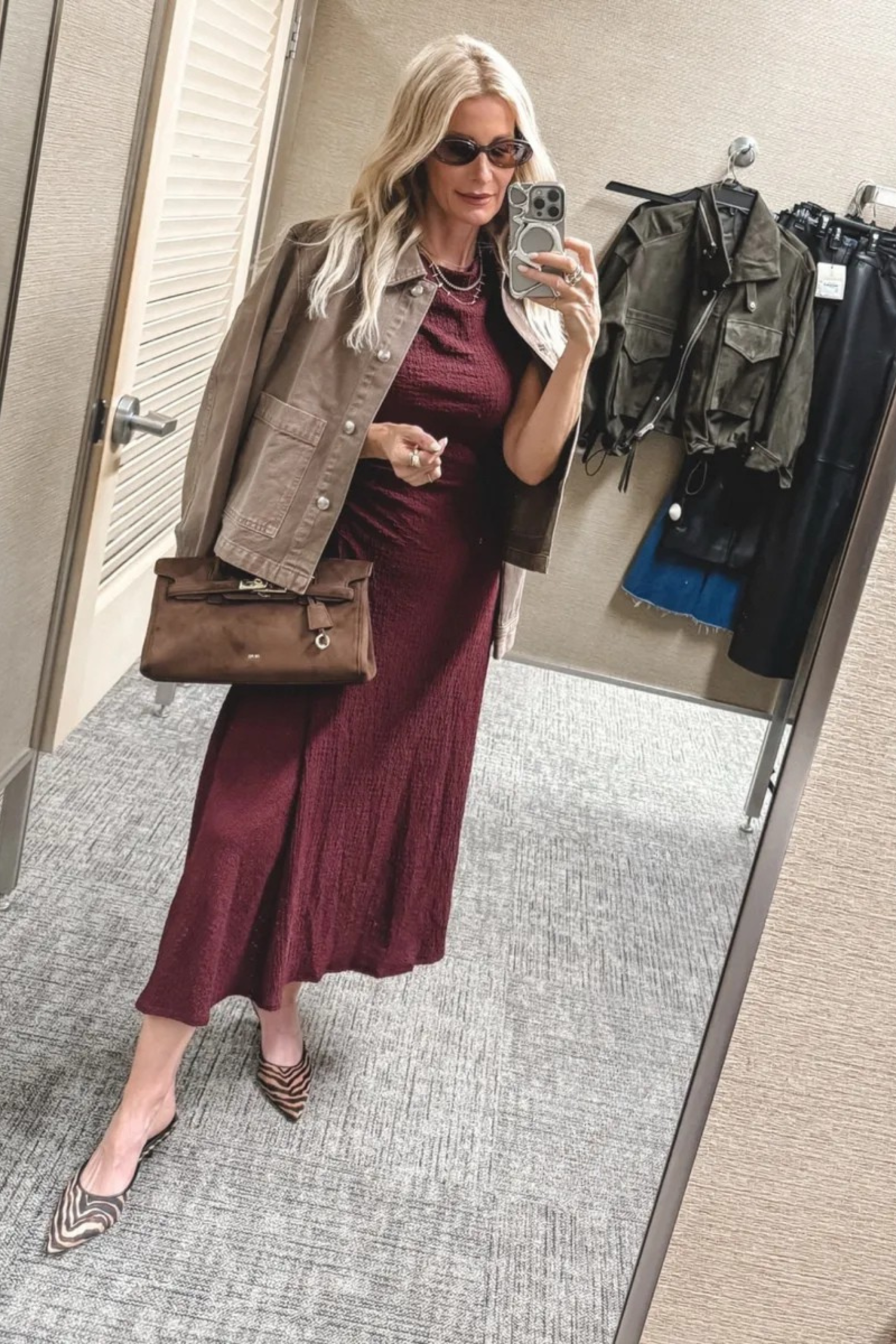 Over 40 fashion icon wearing a burgundy dress with a tan denim jacket.